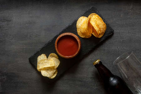 Glass and Bottle of beer with chips and tomato ketchup on dark stone backgroundの写真素材