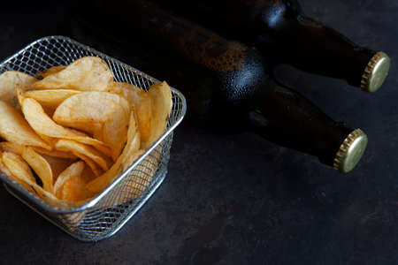 Two Bottles of beer with salted chips on dark stone background