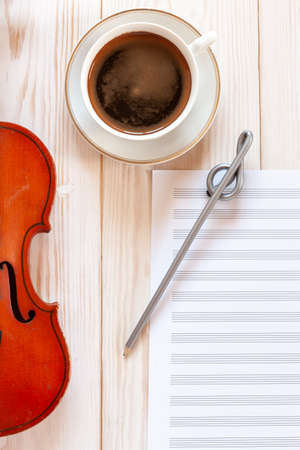 Old violin, pencil treble clef shape, musik note paper and cup of coffee .. Top view, close up, flat lay on white wooden backgroundの写真素材