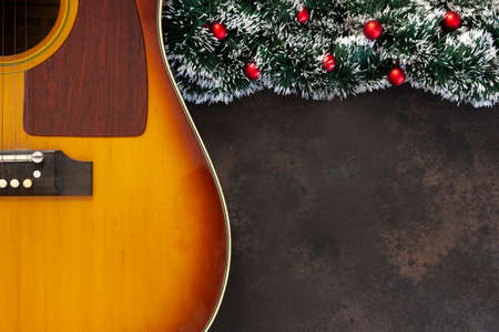 Acoustic guitar and Christmas garland decor with red dekorative balls on dark brown background