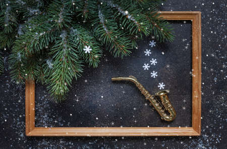 Miniature golden saxophone copy, Christmas tree branches and wooden frame on the blue background with snowflakesの写真素材