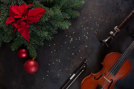 Old violin, fiddlestick and flute with fir-tree branches with Christmas decor and poinsettia. Christmas and New Year's concept. Top view, close-up on dark concrete backgroundの写真素材