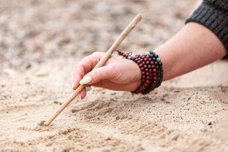 Women Hand with bracelets writing on sand with wooden stick