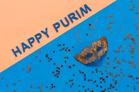 Carnival masquerade mask and gold glitter confetti. Top view, Close up on blue and peach background with Happy Purim text.の写真素材