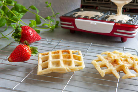 Close-up of waffel maker and soft Viennese waffles on the wire rack with blueberries, strawberry....