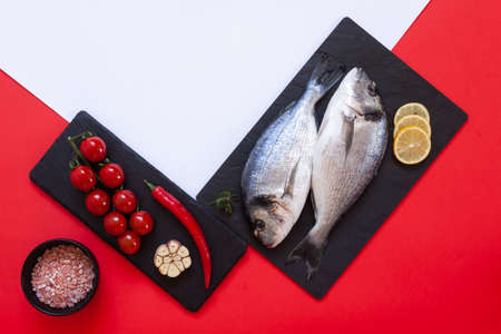 Fresh dorado fish with spices, garlic and seasoning on black cutting board on the white and red...