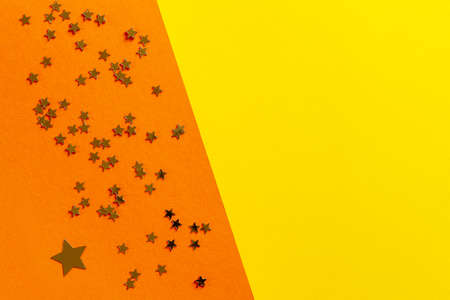 Close up photo of star shape golden glitter confetty on colorful yellow and orange background. Top view, spring, Easter and various holidays and events conceptの写真素材