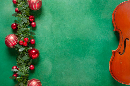 Old violin and beautiful red Christmas decoration on green background. Christmas, New Year's concept. Top view, close-up.の写真素材