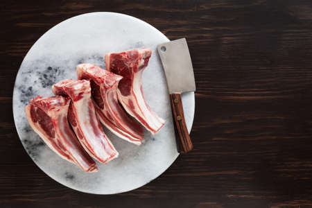 Fresh raw lamb on ribs on stone marble kitchen board on dark wooden backgroundの写真素材