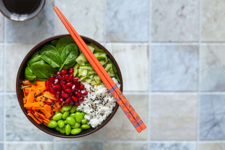 Pan Asian trendy Homemade vegetarian Poke Bowl with Rice, edamame, fresh vegetables and soy sauce, served with chopsticks on ceramic tile background.の写真素材