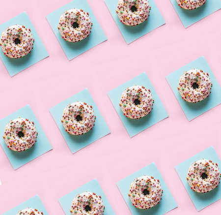 Delicious glazed donuts on the pink table background. Repeating pattern, top view, close up.