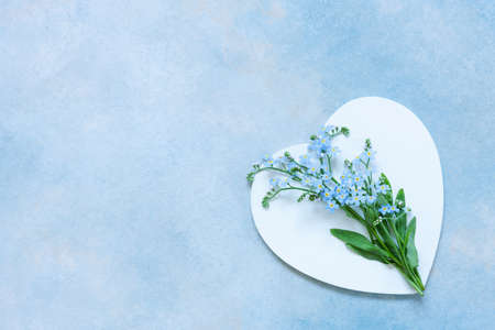 A delicate bouquet of spring fresh forget-me-not flowers is on white heart shape on the blue sky backgroundの写真素材
