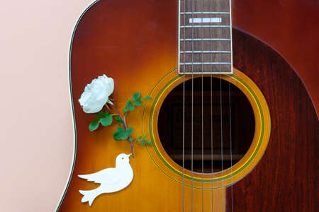 Close up of acoustic guitar and a dove of peace with a white rose in its beak on pastel background. Top view, close up, copy space.の写真素材