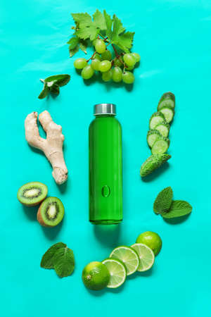 Colorless immunostimulating drink mix in a transparent glass bottle and fresh ingredients fruits and vegetables in green color on a green backgroundの写真素材