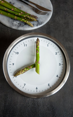 Alarm clock asparagus clock hands and plate with fresh green asparagus, Intermittent fasting...