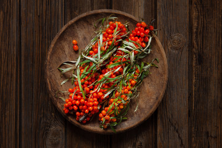 Fresh juicy orange sea buckthorn berries with leaves on a vintage wooden platter, top view on a wooden backgroundの写真素材