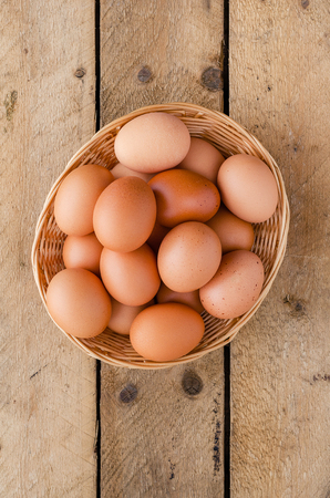 Red chicken eggs in a basket on a wooden, old, rustic table.の写真素材