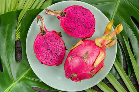 Dragon fruit on a green plate. Dark background with palm leaves.の写真素材