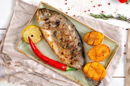 Baked dorada with potatoes on a green dish on a light background.の写真素材