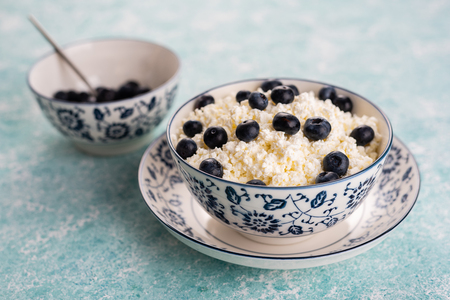 Cottage cheese with blueberries in a porcelain plate on a turquoise vintage background.の写真素材