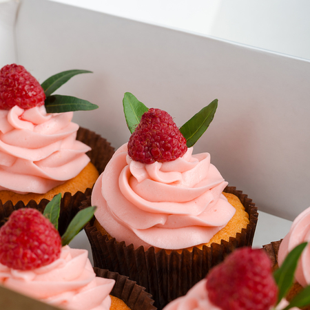 Cupcakes with raspberry cream, decorated with raspberries on top on gift wrap.の写真素材