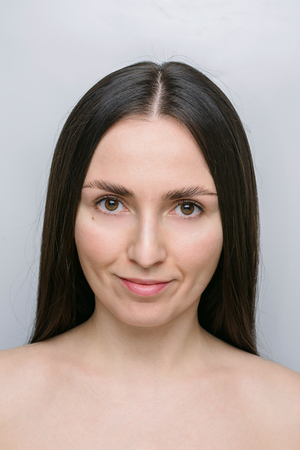 A beautiful young woman, brunette, brown-eyed with straight hair, smiling, no makeup. Studio portrait on gray background.の写真素材