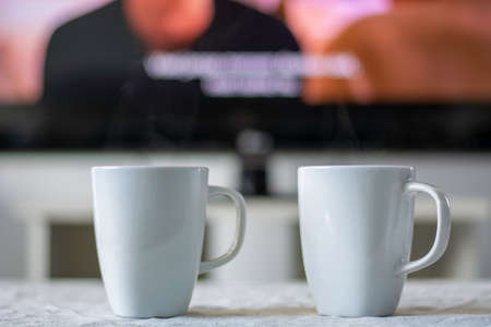 Coffee mugs with a television screen with a movie and subtitles in background. の写真素材