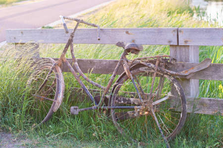 An old abandoned rusty bike parked against a wooden fence. Old fashioned classic bicycle stands forgotten along a bicycle path. の写真素材