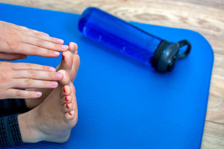 Woman practicing yoga, doing paschimottanasana exercise, Seated forward bend pose. Feet with pink pedicure of woman and water bottle on blue mat. Side view. Concept of indoor workout, exerciseの写真素材