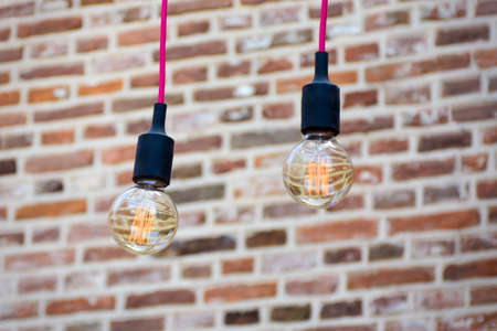 Two glowing light bulbs hanging outside, against a old brick wall