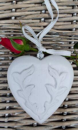White wooden heart and red rose bud on wicker basketの写真素材