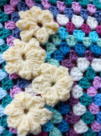 Four yellow crocheted flowers on a handmade blanketの写真素材