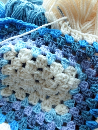 blue and cream crocheted afghan blanket with metal crochet hook and balls of woolの写真素材