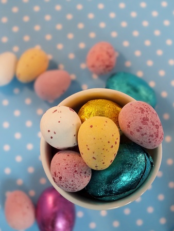 Mini easter eggs in an egg cup with spilled eggs on blue polka dot backgroundの写真素材