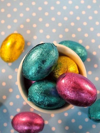 Mini easter eggs in an egg cup with spilled eggs  on blue polka dot backgroundの写真素材