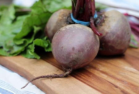 Three beetroots tied in a bunch, organic red vegetable on a wooden chopping board, with leaves, in...