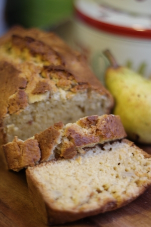 Home made pear and ginger loaf, sliced on kitchen wooden board, ripe pear and cake tins in background, shallow depth of field の写真素材