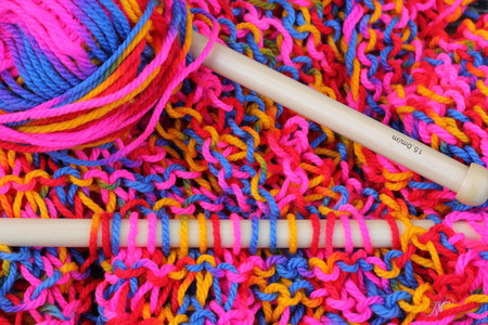 Wooden chunky knitting needles making a stocking stitch multi colored wool garment