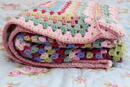 Pretty handmade crochet afghan blanket folded  on bed, made in yarn in shades of pink, cream, purple and greenの写真素材