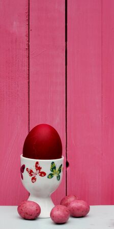 red dyed easter egg in a butterfly patterned  egg cup pink candy eggs background of painted pink wooden boardsの写真素材