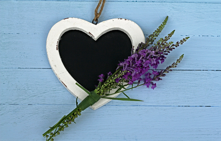 Heart shaped chalk board with purple toad flax flowers ,laying on blue painted floor boards の写真素材