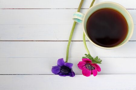 Green tea cup with pink and purple anemones on white wooden plank table , seen from above , mother's day , relaxing natural drinkの写真素材
