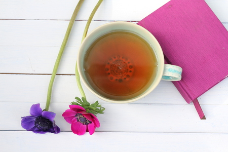 Green tea cup with pink and purple anemones and fuschia note book on white wooden plank table , seen from above , mother's day , thank you gift, relaxing natural drinkの写真素材