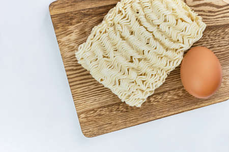 One Dried instant noodles and egg on wooden board