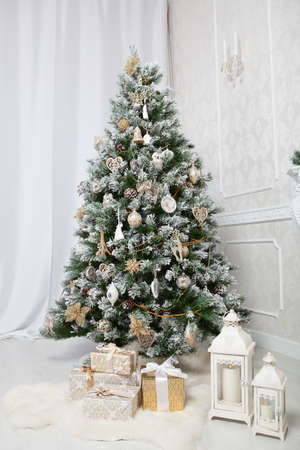 Decoration Christmas tree with with balls, golden flowers, presenrs, white furs and candlesticks in studio interiorの写真素材
