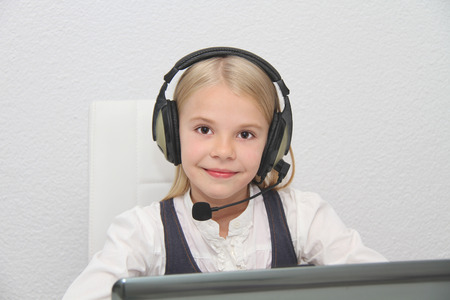 Llittle girl sits in front of a laptop with headphones and learning