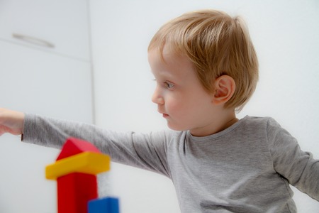 Little boy three years old sits on the table and plays with plasticine and wooden and plastic toys, cubes and diceの写真素材