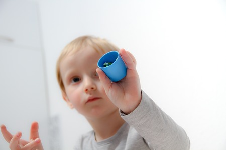 Little boy three years old sits on the table and plays with plasticine and wooden and plastic toys, cubes and diceの写真素材