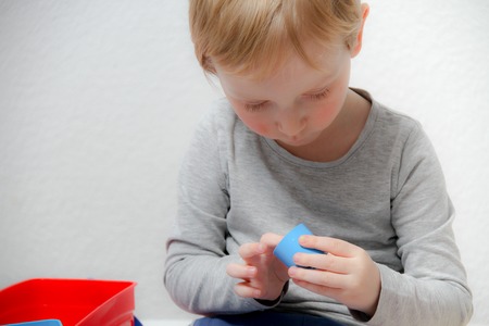 Little boy three years old sits on the table and plays with plasticine and wooden and plastic toys, cubes and diceの写真素材