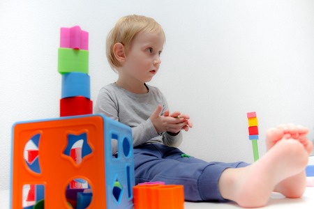 Little boy three years old sits on the table and plays with plasticine and wooden and plastic toys, cubes and diceの写真素材